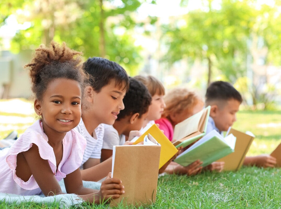 group of kids reading books and enjoying themselves in a park outside