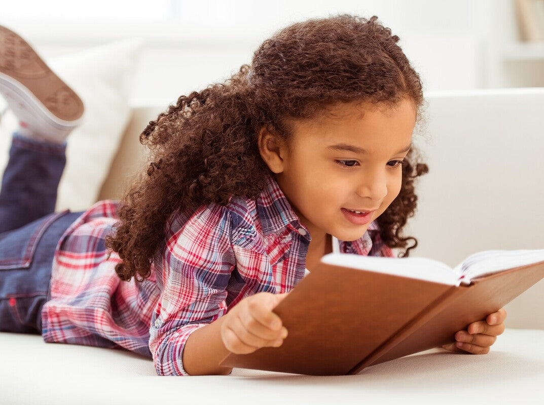 young girl reading a book on the floor after learning how to improve kids’ reading