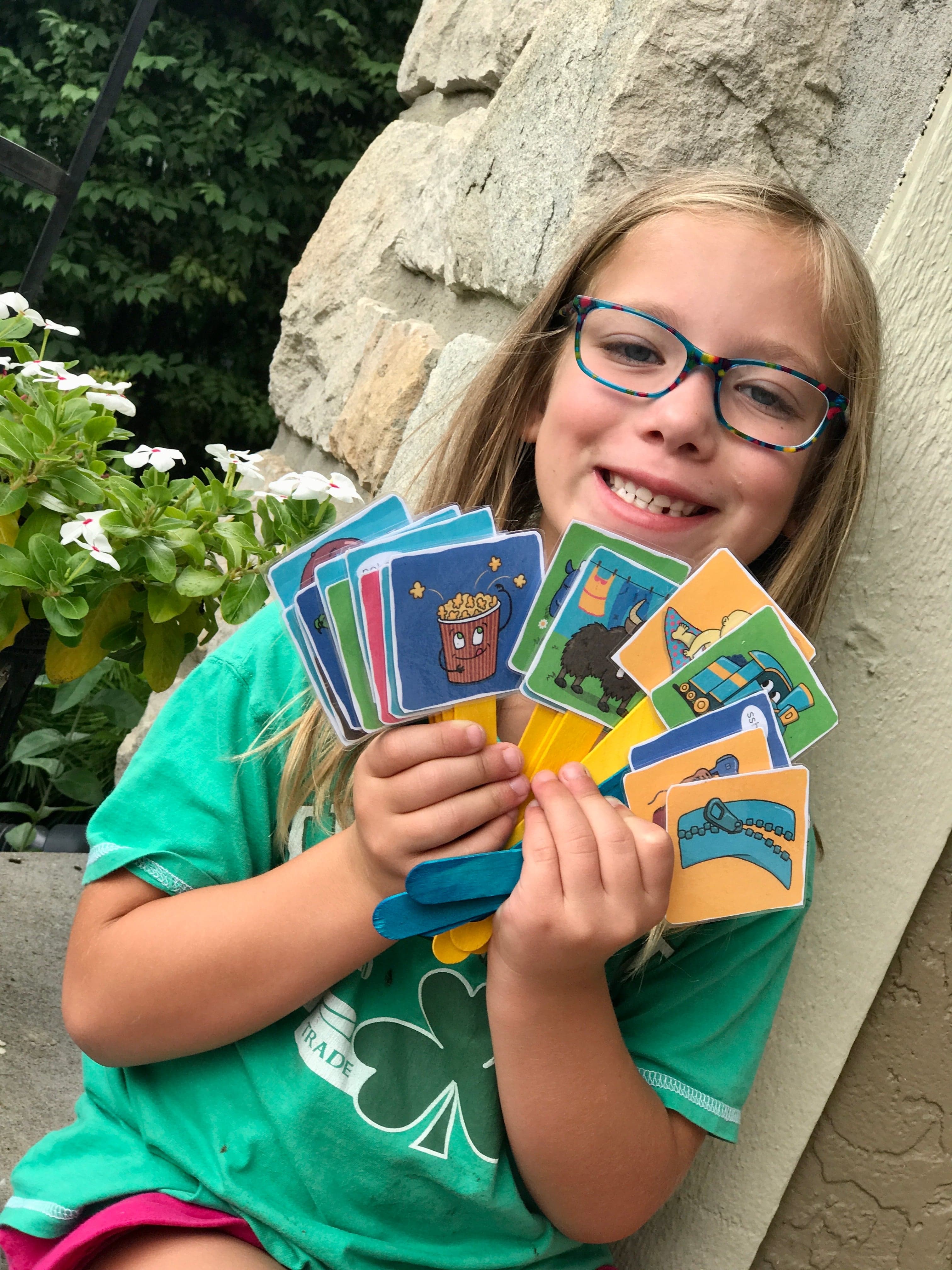 Girl smiling, holding a stack of colorful cards.