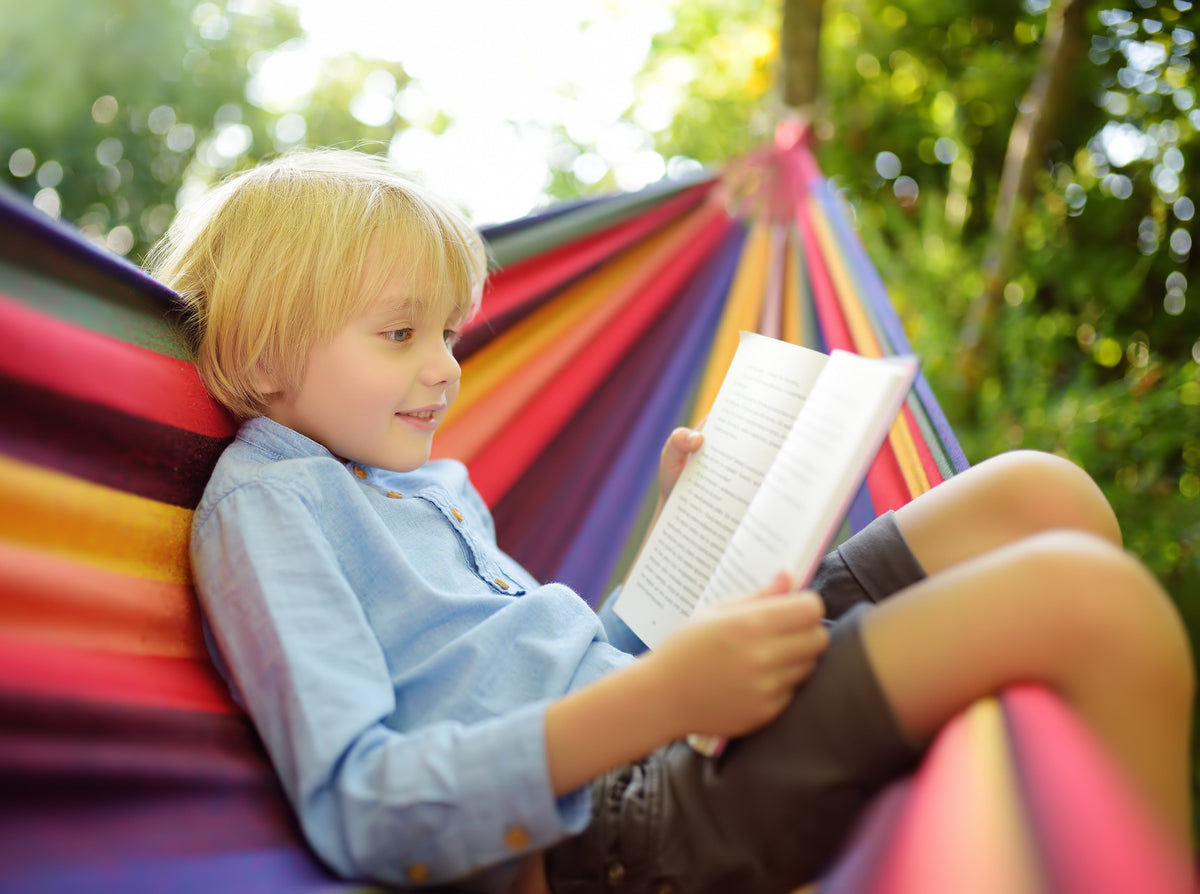 young boy enjoying a book outside after his parents learned how to help my child with reading comprehension